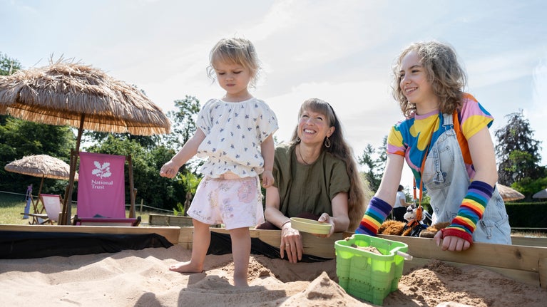 A young child playing in a sandpit with family members at Chirk Castle.